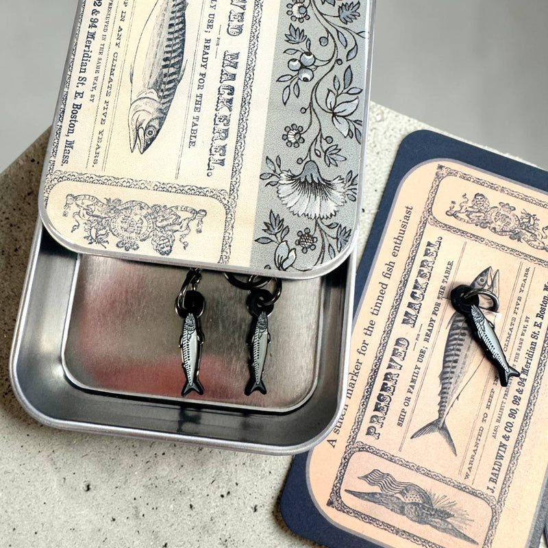 Metallic fish-shaped earrings in a decorative tin with vintage-style packaging.