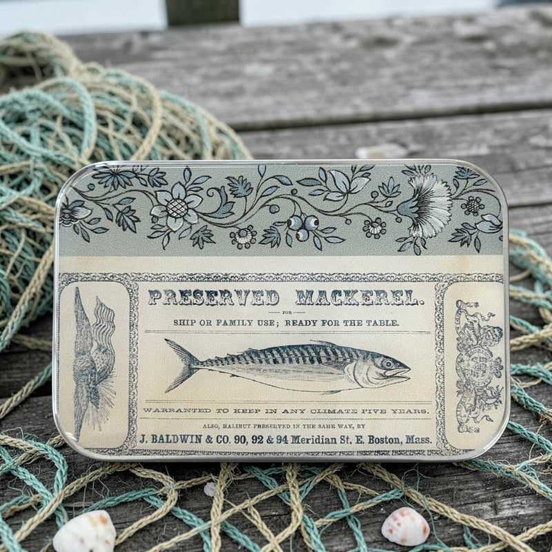 Vintage-style tin labeled 'Preserved Mackerel' on a wooden surface with fishing net and shells.